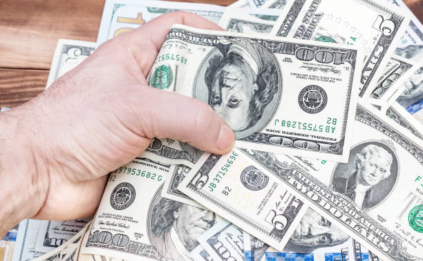 istock Man's hand holds dollar bills over table with money. 924972020