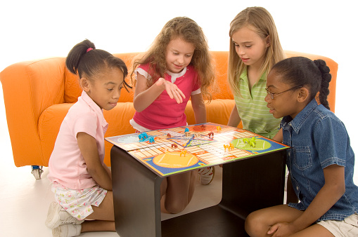 four young girls play a board game. All recognaizable parts of the game have been altered to avoid copyright problems.