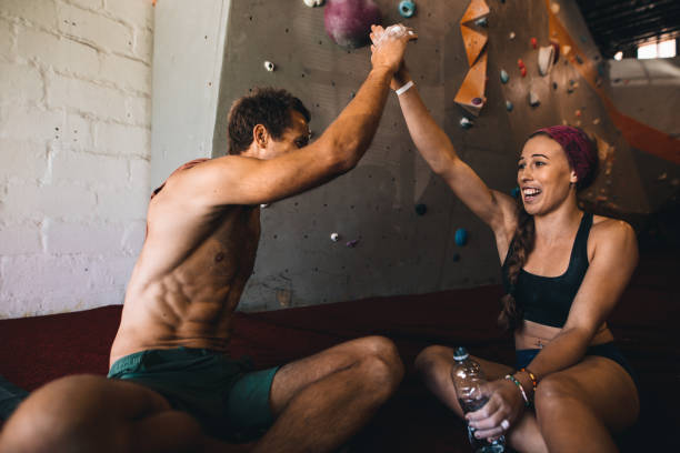 Man and woman rock climbers giving high five after successfully completing wall climbing. Happy rock climbing couple relaxing after work out.