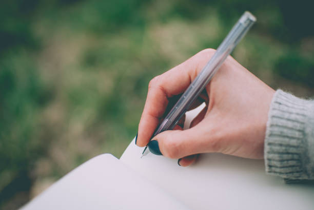 istock Tender girl's pale hand writing in notebook with blank pages. 924989064