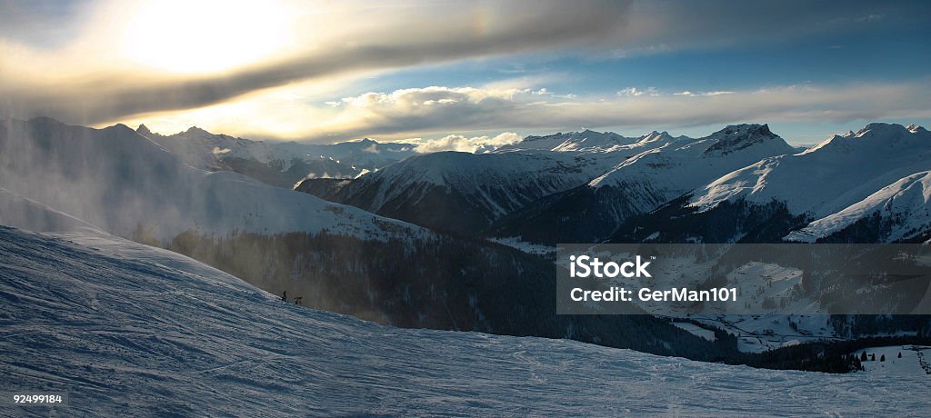 Downhill run Ski slope in Davos, Switzerland at sunset. Captured some snow thrown into the air by a passing skier. Cloud - Sky Stock Photo