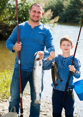 Positive father and son fishing with rods in summer day