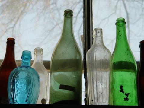 View from below of a white man hand throwing a glass bottle on a recycle bin. Image taken from the interior of the trash bin and against the sky.