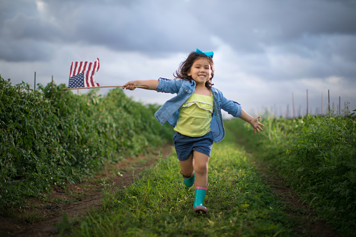 Little girl on vegetable field running with an american flag