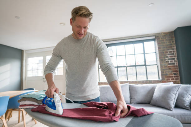 przystojny samotny facet w domu prasowanie jego ubrania patrząc szczęśliwy - iron laundry cleaning ironing board zdjęcia i obrazy z banku zdjęć