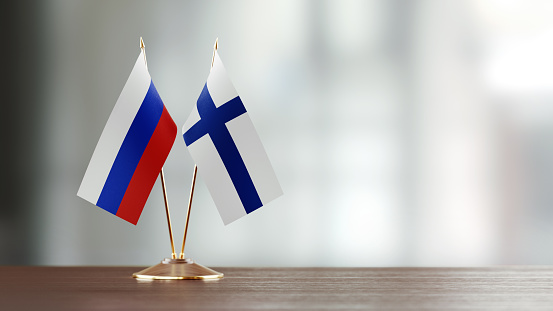 Russian and Finnish flag pair on desk over defocused background. Horizontal composition with copy space and selective focus.