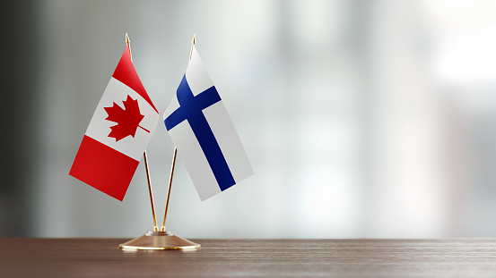 Canadian and Finnish flag pair on desk over defocused background. Horizontal composition with copy space and selective focus.