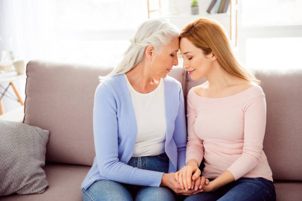 concepto de belleza de calidez comodidad maternidad paternidad. perfil de lado dado vuelta medio foto abuelita cierre delicada encantador linda y nieta sentados juntos en el diván tocar frente - aging process women human face daughter fotografías e imágenes de stock