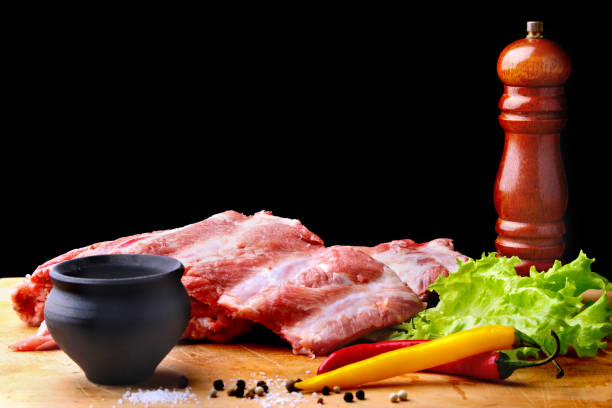 istock Raw Ribs on a rustic cutting board with salt, pepper and grinder for spices . Black Background for copy space. Top View. 925040484
