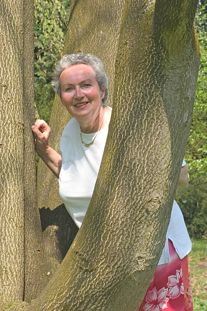 kobieta w jej sixties patrząc wokół drzewa - senior adult close to moving up togetherness zdjęcia i obrazy z banku zdjęć