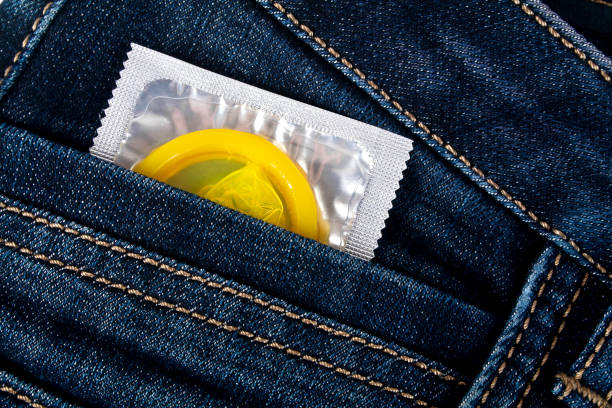 préservatif jaune dans une poche de jeans bleu - sex condom jeans horizontal photos et images de collection