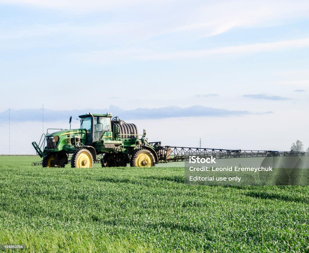 Tractor with a spray device for finely dispersed fertilizer. Fields near the Temryuk, Russia - May 01, 2017: Tractor with high wheels is making fertilizer on young wheat. The use of finely dispersed spray chemicals. Tractor with a spray device for finely dispersed fertilizer. Tractor on sunset background. Agricultural Field Stock Photo