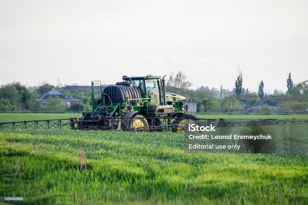 Tractor with a spray device for finely dispersed fertilizer. Tractor on the sunset background. Tractor with high wheels is making fertilizer on young wheat. The use of finely dispersed spray chemicals Fields near the Temryuk, Russia - May 01, 2017: Tractor with high wheels is making fertilizer on young wheat. The use of finely dispersed spray chemicals. Tractor with a spray device for finely dispersed fertilizer. Tractor on sunset background. Agricultural Field Stock Photo