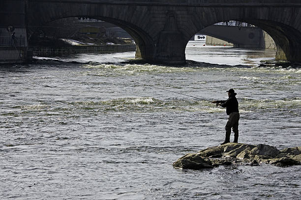 Fishing in the downtown Stockholm Silhouette of man fishing on a rock in the middle of downtown Stockholm, in early spring with water from melting ice in the background. strommen stock pictures, royalty-free photos & images