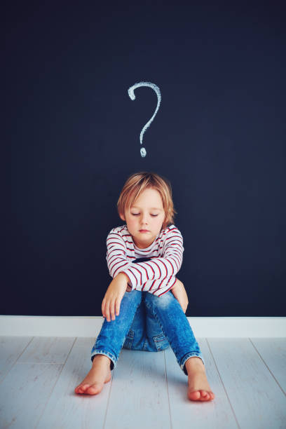 istock sad, frustrated school boy sitting on the floor with question mark above him 925082506