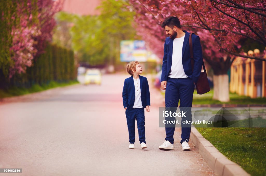 happy father and son walking together along blooming spring street, wearing suits Father Stock Photo