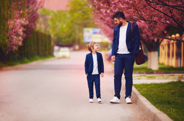 happy father and son walking together along blooming spring street, wearing suits happy father and son walking together along blooming spring street, wearing suits fashionable dad stock pictures, royalty-free photos & images