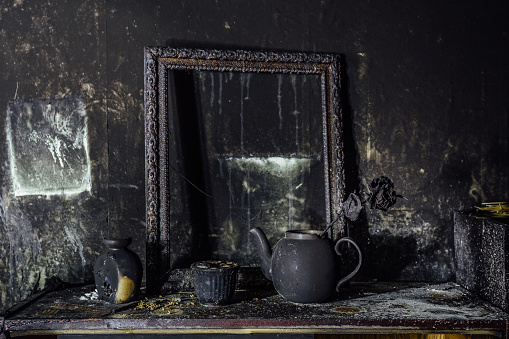 Burnt room interior. Burnt still life. Charred wall, picture frame, pot with burned rose in black soot.