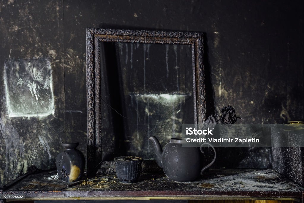 Burnt room interior. Burnt still life. Charred wall, picture frame, pot with burned rose in black soot Burnt room interior. Burnt still life. Charred wall, picture frame, pot with burned rose in black soot. Damaged Stock Photo