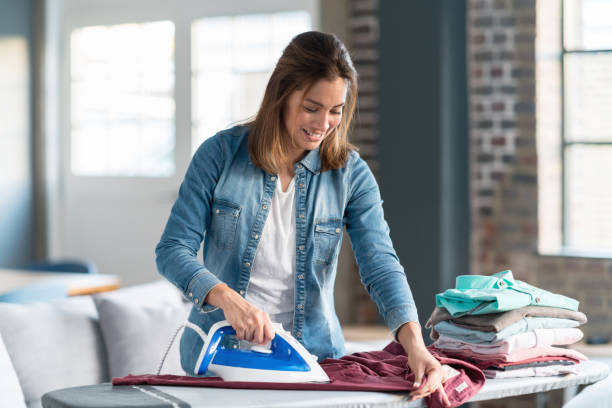 feliz mujer planchando su ropa en casa - iron fotografías e imágenes de stock