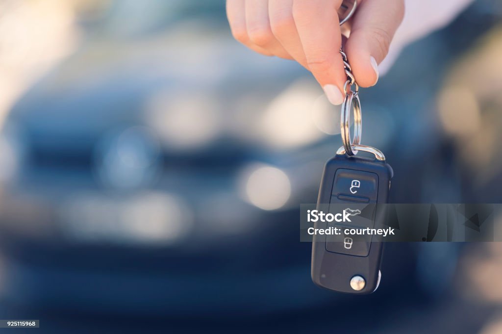 Female car salesperson handing  over the new car keys. Female car salesperson handing  over the new car keys. There is a new car behind her out of focus. Close up with Copy space Car Stock Photo