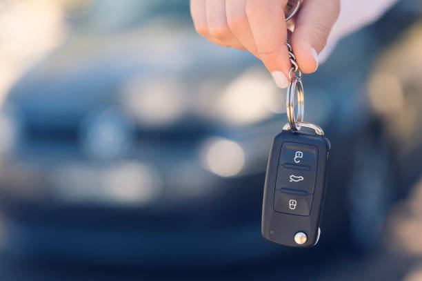 Female car salesperson handing  over the new car keys. Female car salesperson handing  over the new car keys. There is a new car behind her out of focus. Close up with Copy space car key photos stock pictures, royalty-free photos & images