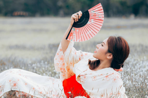 Asian girl wearing a kimono carrying holding fan on a green grass