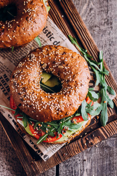 pãezinhos com creme, abacate, tomate e rúcula em fundo de tabuleiro e mesa de madeira. café da manhã saudável. vista superior e espaço de cópia - bun sandwich vegetable cream cheese - fotografias e filmes do acervo