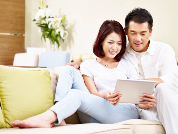 istock asian couple sitting on couch looking at digital tablet 925133160