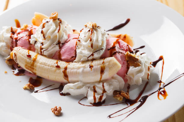 Vanilla ice cream waffle banana with chocolate sauce and mint leaf decorate on top  serve on white plates over the white wooden table