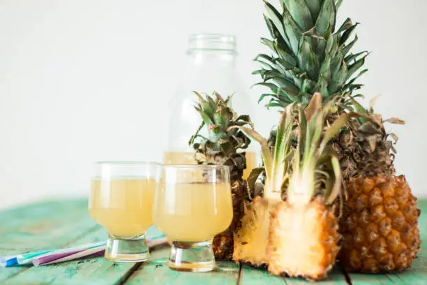 Photo of Pineapple slices and juice in glassware on wooden table, healthy detox food