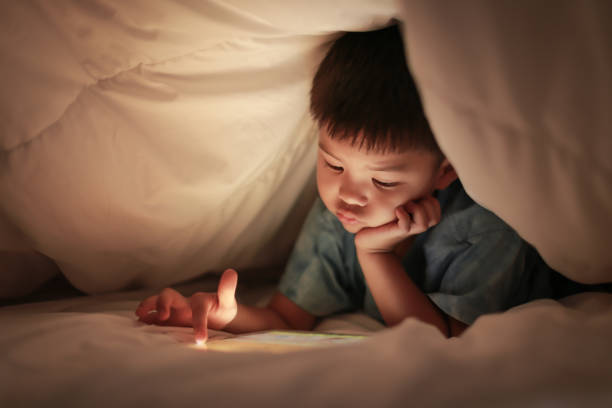 istock Kid play internet online game, under duvet. 925159432