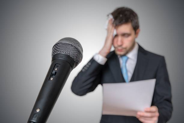 istock Nervous man is afraid of public speech and sweating. Microphone in front. 925159708