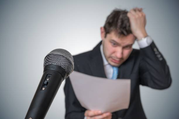 istock Nervous man is afraid of public speech and sweating. Microphone in front. 925159716