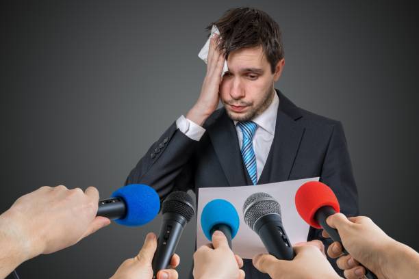 istock Nervous man is afraid of public speech and sweating. Many microphones in front. 925159720