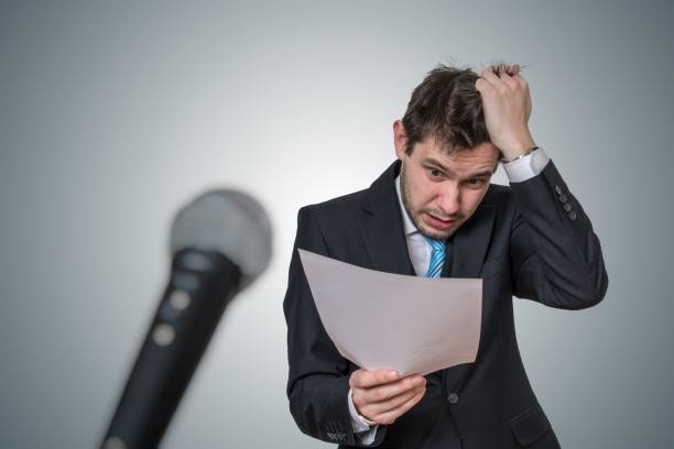 istock Nervous man is afraid of public speech and sweating. Microphone in front. 925159764