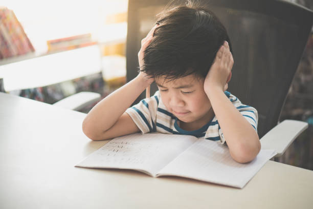 Asian child working on hard homework Unhappy Asian child working on hard homework at home alone asian kids learning stock pictures, royalty-free photos & images