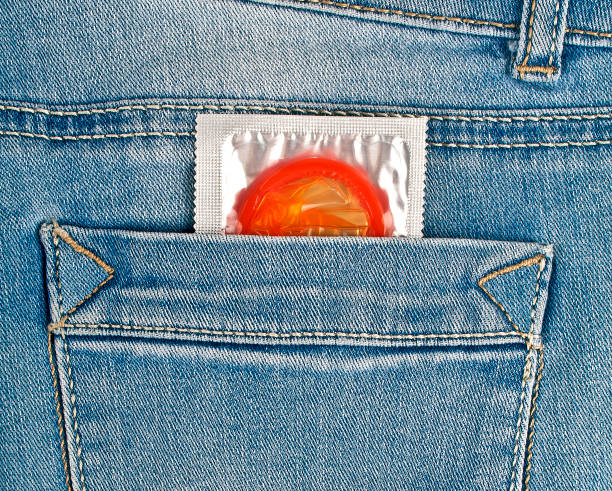 préservatif rouge dans la poche de jeans bleu - sex condom jeans horizontal photos et images de collection