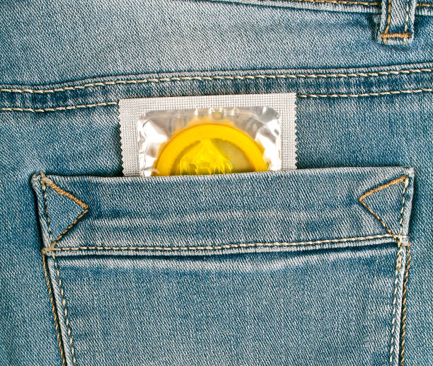 préservatif jaune dans la poche de jeans bleu - sex condom jeans horizontal photos et images de collection