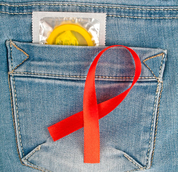 préservatif jaune dans la poche de jeans bleu et le ruban rouge sida sensibilisation - sex condom jeans horizontal photos et images de collection