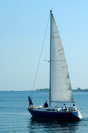 4 passengers aboard a sailboat with all logos and names removed and all persons with backs turned to camera or backlit to be recognizable.