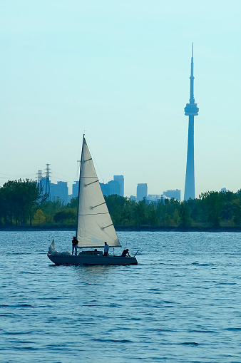 A sailboat passing by the Toronto shoreline with all persons backlit to be recognizable and all logos and registrations removed.