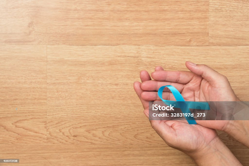 Men's health care concept. Man hands holding Light blue, sky blue ribbons, on wooden background, Prostate Cancer Awareness and Adrenocortical carcinoma awareness. Prostate Gland Stock Photo