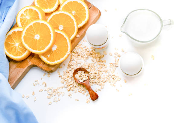 Oat flakes plate with milk, orange, eggs on a wooden white table. Top view of healthy oat flakes breakfast. Copy space