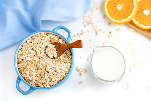 Oat flakes plate with milk, orange, eggs on a wooden white table. Top view of healthy oat flakes breakfast. Copy space. blue napkin Breakfast in bed plate, breakfast table buffet. Healthy ingredients