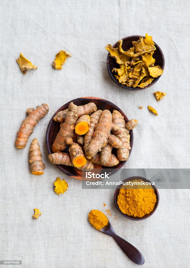 Fresh and dried turmeric roots in a wooden bowl. Grey textile background. Top view. Turmeric Stock Photo