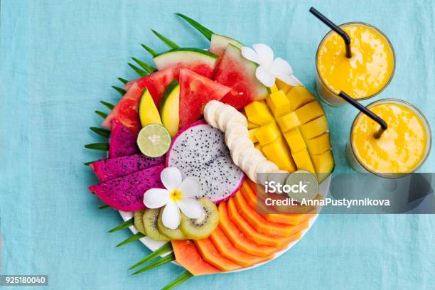 Photo libre de droit de Assortiment De Fruits Tropicaux Sur Une Plaque Blanche Avec Feuille De Palmier Arbre Avec Smoothie Mangue Fond Bleu De Textile Vue De Dessus Espace Copie banque d'images et plus d'images libres de droit de Tropical