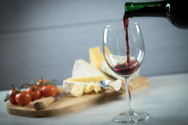 Red wine poured into a glass with cheese board stock photo