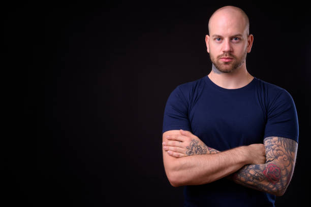 istock Young handsome bearded bald man with tattoos against black background 925183856