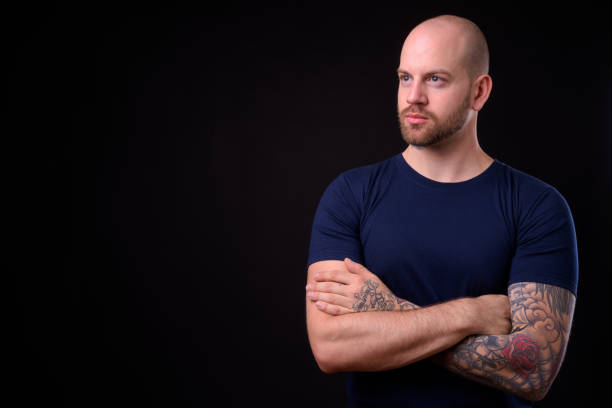 istock Young handsome bearded bald man with tattoos against black background 925183900